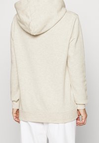 Sudadera beige claro con vista completa por la parte de atrás, que presenta una capucha amplia y mangas largas, hecha de una suave mezcla de algodón texturizado.