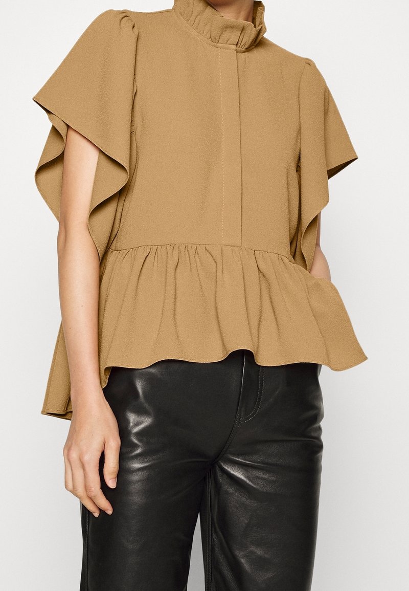 Top peplum marrone aderente con maniche a volant, scollo alto e tessuto testurizzato; abbinato a pantaloni neri lucidi a sigaretta.