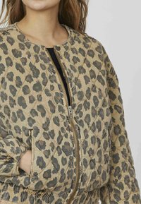 Quiltet bomberjakke i beige med mørkt leopardprint, som har en frontlynlås, sidelommer og elastiske cuffs.