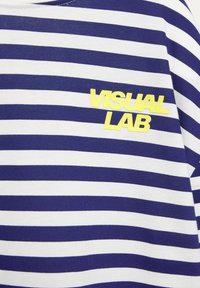 Kék és fehér csíkos anyagú póló, sárga "VISUAL LAB" logóval a mellrészen. Puha pamut textúra, klasszikus kerek nyakú dizájn.