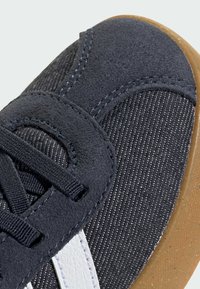 Semišové a textilní tenisky s tmavě šedým svrškem, bílými bočními pruhy a hnědou gumovou podrážkou. Obsahují texturovaný povrch a šněrování.