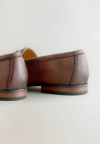 Braune Lederschuhe mit strukturiertem Finish, kleinem Absatz und einer kontrastierenden gestreiften braunen und schwarzen Sohle. Dezente Nähte sind sichtbar.