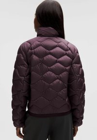 Fioletowa pikowana kurtka puchowa z wysokim kołnierzem, charakteryzująca się smukłym krojem, błyszczącą fakturą oraz elastycznymi mankietami i dołem.