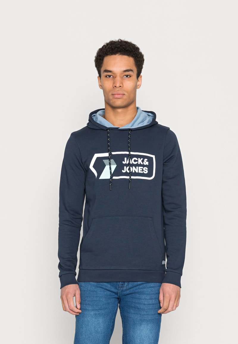 Felpa blu navy con una fodera della cappuccio di un blu chiaro. Presenta una grande grafica bianca "JACK & JONES", cordini regolabili e una tasca frontale.