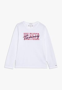 Biała koszulka z długim rękawem z wyraźnym różowym i granatowym logo "Tommy Hilfiger". Prosty fason z okrągłym dekoltem i standardowym krojem.