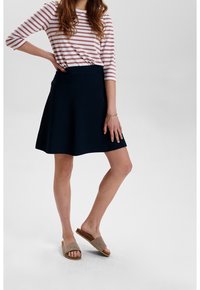 Merenkatuinen flare-hame, jossa on sileä pinta, yhdistettynä vaaleanpunaisiin ja valkoisiin raidoitettuihin paitoihin. Mallilla on päällään ruskeat ristikkäishenkiset sandaalit.