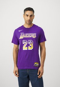 Violet medvilninė marškinėliai su "LAKERS" užrašu baltos ir geltonos spalvos, skaičius "23" baltos ir geltonos spalvos bei logotipo užrašas ant apykaklės. Yra Nike ženklas.