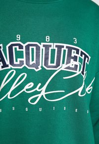 Sudadera verde con una gran impresión gráfica en azul marino y blanco que incluye el texto "ACQUET" y "Valley Club". Fabricada con una mezcla de algodón texturizado.