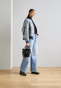 Chaqueta bomber floral, top negro, vaqueros de pierna ancha azul claro, botas negras hasta el tobillo y un pequeño bolso negro con detalles en dorado.