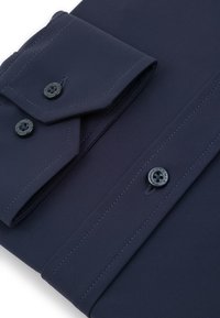 Granatowa koszula z dwoma czarnymi guzikami przy mankietach, o gładkiej fakturze i kołnierzykiem w szpic z precyzyjnymi szwami.
