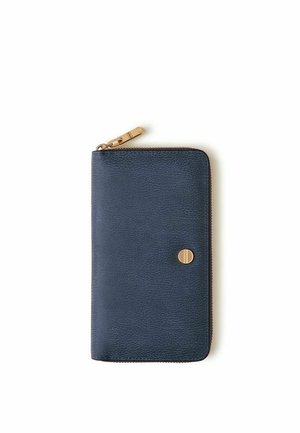 Portefeuille en cuir bleu marine avec fermeture éclair dorée et petit emblème rond doré sur fond blanc, fermé et posé à plat.