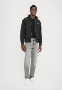 Sort bomberjakke med lynlås foran og ståkrave, lagd over en sort skjorte. Bæres med lysegrå jeans og hvide sneakers.