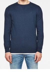 Náměsíčná modrá svetr s kulatým výstřihem a dlouhými rukávy, pletená textura, a žebrované akcenty na výstřihu a lemu. Malé logo na prsou.