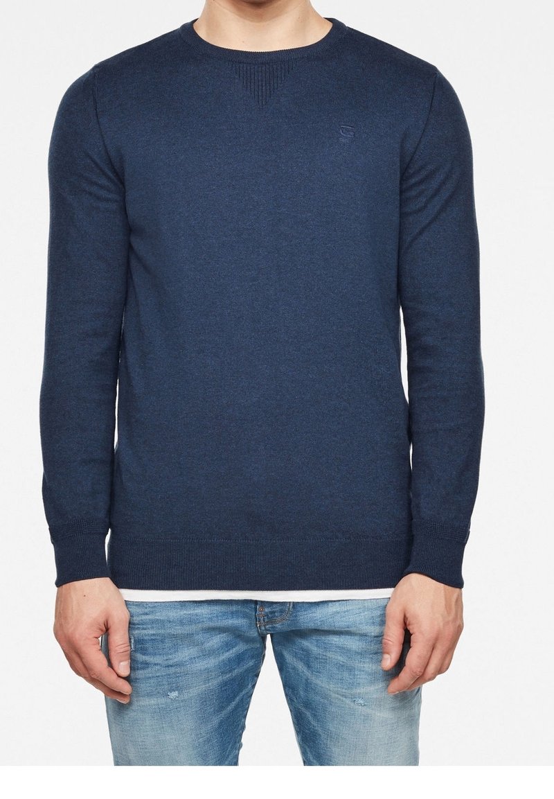 Náměsíčná modrá svetr s kulatým výstřihem a dlouhými rukávy, pletená textura, a žebrované akcenty na výstřihu a lemu. Malé logo na prsou.