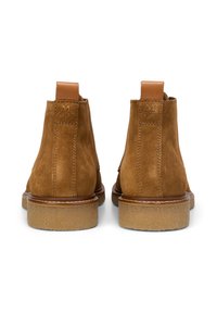 Bottes cheville en daim marron avec languettes en cuir, semelles en caoutchouc beige et surface légèrement texturée. Des coutures verticales longent l'arrière.