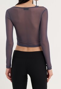 Långärmad, genomskinlig marinblå topp med en kortad design, slät textur och rundad halsringning, kombinerad med svarta stretchleggings.