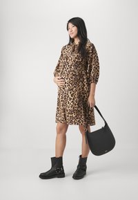 Robe imprimée léopard avec taille à cordon, manches bouffantes longues, bottes noires jusqu'à la cheville avec boucles, et sac à épaule noir.