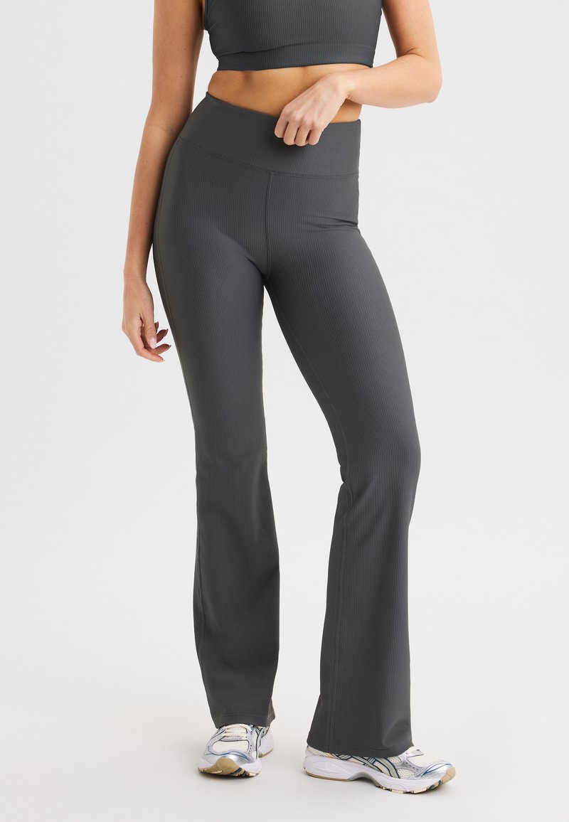 Grijze geribbelde flared leggings met een hoge tailleband. Heeft een gladde textuur en een strakke pasvorm. Draagt met wit en grijze sportschoenen.