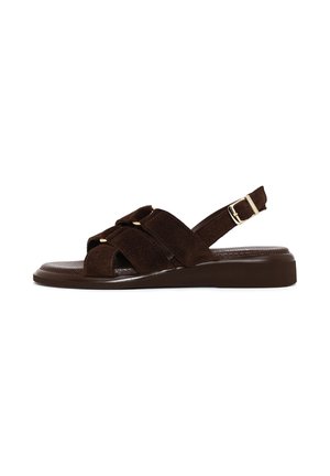 Bruine suède platte sandaal met gekruiste bandjes en verstelbare gesp slingback op een gestructureerde zool, zijaanzicht op een witte achtergrond.