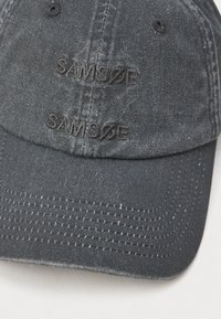 Boné de beisebol em denim preto com a inscrição repetida "SAMSØE" bordada em fio preto no painel frontal.