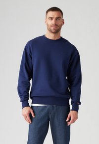 Navyblauwe sweatshirt van katoen, met een ronde hals, lange mouwen, ribbelmanchetten en een klein logo op de borst. Draagt een spijkerbroek.
