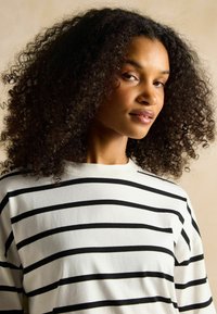 Langärmliges, Rundhalsoberteil in Weiß mit kräftigen schwarzen horizontalen Streifen. Weicher Stoff mit lockerem Schnitt und sichtbaren Nähdetails.