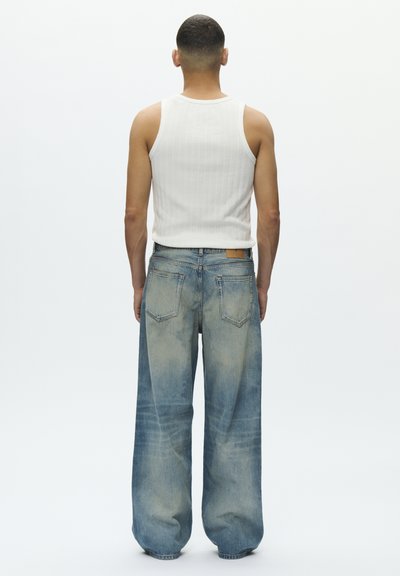 Bredbente jeans i blå denim med falmede partier, femlommers design og en brun lærlap ved linningen. Ribbede hvite tanktop.