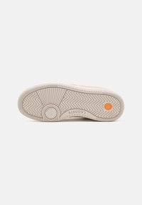 Semelle de chaussure avec des motifs de bande de roulement en zigzag et linéaires, design circulaire près du talon, détail circulaire orange près des orteils et marquage "LACOSTE" sur le côté.