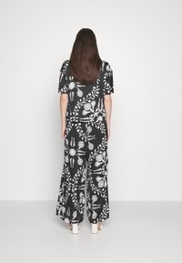 Czarny strój z białymi kwiatowymi wzorami, luźna góra i spodnie z szerokimi nogawkami. Gładka tkanina z krótkimi rękawami i okrągłym dekoltem.