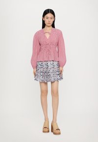 Rød og hvit stripete bluse med knytning i halsen og sammensydd brystparti, sammen med et blått blomstermønstret skjørt. Beige platå sko.