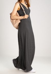 Robe maxi avec des rayures verticales noires et blanches, design en v, associée à un sac à dos beige et des baskets blanches. Tissu lisse, coupe décontractée.