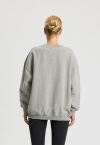 Felpa grigia oversize con scollatura rotonda, spalle scese e orlo a coste. Presenta una texture morbida e una vestibilità casual, abbinata a leggings neri.