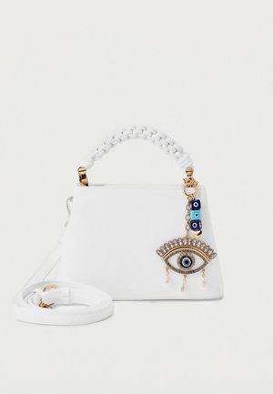 Sac à main blanc avec poignée tressée et bandoulière amovible, orné d'un charm en forme d'œil doré et bleu avec des perles et des perles pendantes.