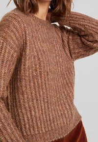 Pull en tricot dans des teintes brunes douces, présentant une texture côtelée, un col rond et une coupe décontractée avec des coutures d'épaules distinctes.