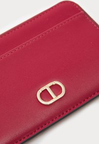 Portafoglio in pelle rossa con accenti in metallo dorato e logo ovale. Texture liscia e dettagli di cucitura a contrasto.