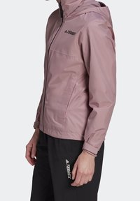 Růžová nepromokavá bunda se zipem, kapucí a elastickými manžetami; na hrudi a boční kapse je logo TERREX.