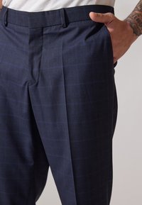 Pantalons à carreaux bleu marine avec une texture douce, dotés d'une coupe ajustée et d'un motif à carreaux subtil, conçus avec des poches avant.