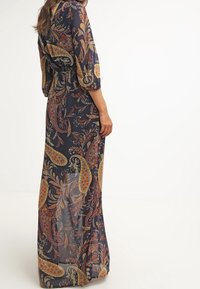 Maxiklänning i genomskinligt tyg med en mörk marina bakgrund, prydd med färgglada paisleymönster och trekvartslånga ärmar.