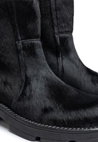 Botines de tobillo de pelo de ternera negro con una textura suave, forma estructurada y suela de goma contrastante. Presentan costuras visibles a lo largo del borde.