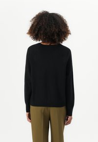 Maglione nero lavorato a maglia con scollatura rotonda e polsini a coste, visto da dietro. Presenta una vestibilità morbida e dettagli di cucitura discreti.