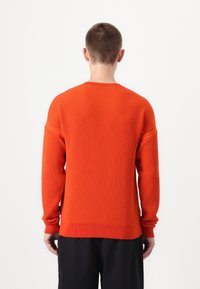 Maglione arancione a coste con scollatura tonda e maniche lunghe. Presenta un tessuto testurizzato e una vestibilità comoda.