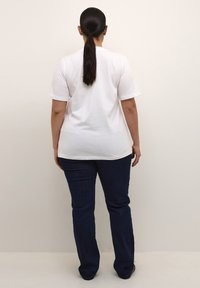 Witte katoenen T-shirt met korte mouwen, gecombineerd met donkerblauwe denim jeans. De jeans zijn strakke pasvorm en hebben een uitlopende beenopening.