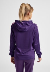 Paarse hoodie met een gladde textuur, met roze accenten op de schouders en lange mouwen, gecombineerd met bijpassende paarse broek.