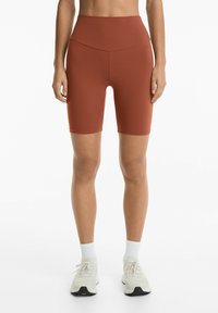 Burgundy cykelshorts med hög midja och sömlös design, slät textur och längd ovanför knäet, som kombineras med ljusa sneakers och ankelsockor.