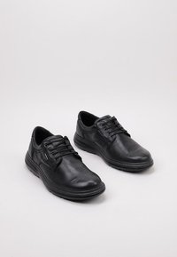 Zapatos de cuero negro con acabado texturizado, puntera redonda y diseño de cordones. Presentan una suela acolchada y acentos mínimos para una apariencia elegante.