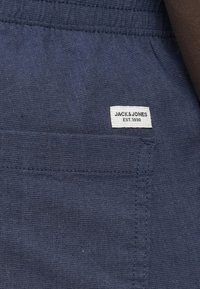Tissu en lin bleu marine avec une surface texturée, doté d'une étiquette blanche portant l'inscription "JACK & JONES EST. 1990" et d'un détail de poche cousue.