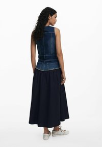 Denim sleeveless top with a fitted silhouette, paired with a long, flowing navy skirt. The skirt features a gathered waist and casual sneakers.