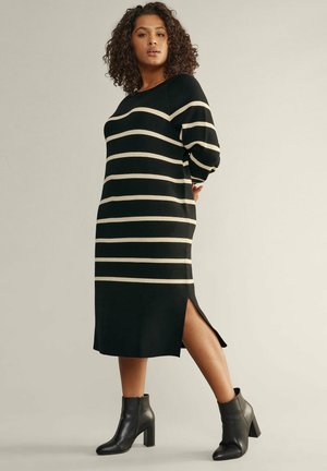 Stribet sweaterkjole i sort og creme med rund halsudskæring, lange ærmer, sideslidser og båret med sorte hælede ankelstøvler.