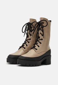 Bottines en cuir beige à lacets avec une semelle plate-forme noire épaisse, présentant un bout rond, des lacets noirs et des détails de couture contrastants.