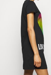 Czarna bawełniana sukienka w formie t-shirtu z krótkimi rękawami, z grafiką stopniowanego serca w kolorach różowym, zielonym i żółtym oraz białym napisem "LOVE ME".